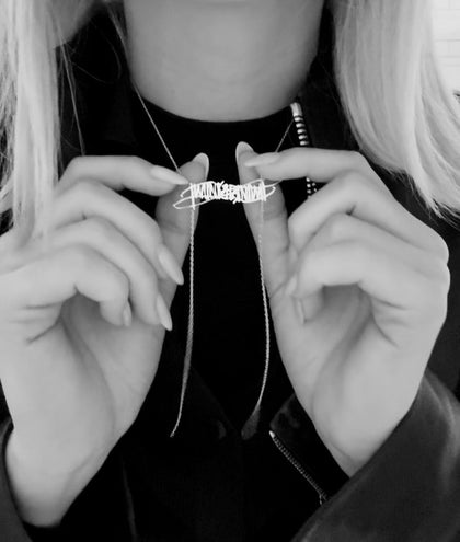 Brenda hashtag holding the timing necklace with her nails wearing a black t-shirt 
